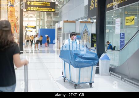 BANGKOK THAILAND APR 14 2021 der Arbeiter trägt eine OP-Maske und drückt die Hand auf den Wagen der Ausrüstung für die Reinigung am Flughafen. Stockfoto