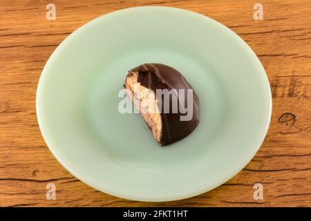 Halb verzehrtes, mit Schokolade übersätes, kuppelförmiges Bonbon mit Zuckerkeks, Cappuccino-Gelee und Schlagsahne auf grünem Dessertteller Stockfoto