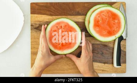 Wassermelonenscheiben auf Holzschneidebrett, flach liegend, Frauenhände Stockfoto