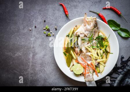 Gedünsteter Fisch auf weißem Teller mit Ingwer-Chili-Kraut und Gewürzen Zitronenlime auf dunklem Hintergrund, gedünsteter Zackenbarsch mit Sojasauce im chinesischen Speisestil Stockfoto