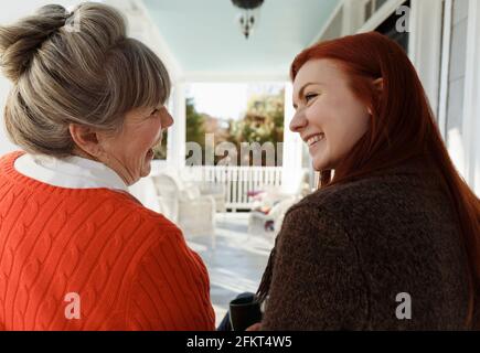 Ältere Frau und Erwachsene Tochter lachen und unterhalten sich auf der Veranda Stockfoto