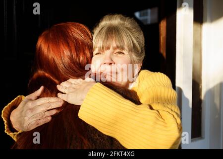 Rückansicht einer älteren Frau und einer erwachsenen Tochter, die sich an der Eingangstür umarmten Stockfoto