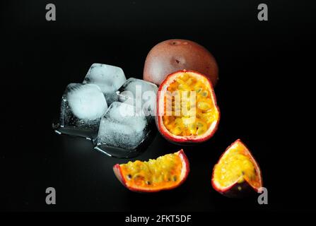 Schneiden Sie reife Früchte exotischer Passionsfrucht neben geschmolzenen Eiswürfeln auf schwarzem Hintergrund. Nahaufnahme. Stockfoto