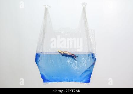 Plastiktüte mit verschwommenem Schildkröten-Spielzeug-Modell in Wasseroberfläche auf weißem Hintergrund. Minimales Konzept für den Weltmeere-Tag. Stockfoto