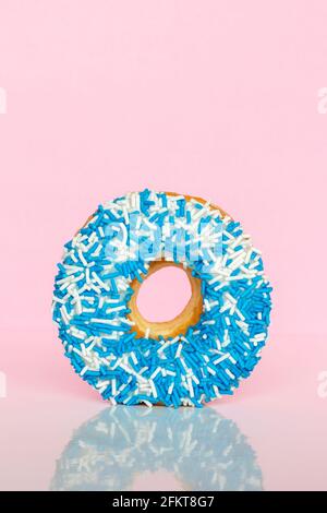 Donut mit blauen und weißen Streuseln auf rosa Hintergrund mit Reflexion und Kopieplatz für Text. Stockfoto