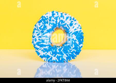 Donut mit blauen und weißen Streuseln auf gelbem Hintergrund mit Reflexions- und Kopierfläche für Text. Stockfoto