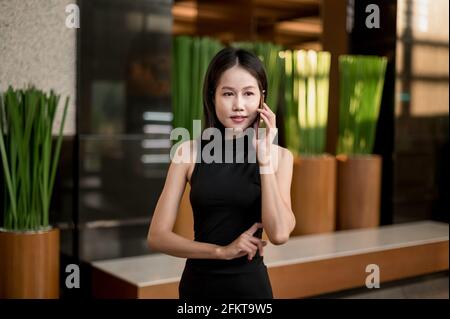 Die junge Geschäftsfrau aus asiatischer Ethnie spricht in Innenräumen über ihr Mobiltelefon. Stockfoto