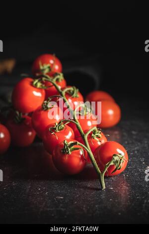 Frische rote Kirschtomaten. Kleine Tomaten auf Ast auf schwarzem Tisch. Stockfoto