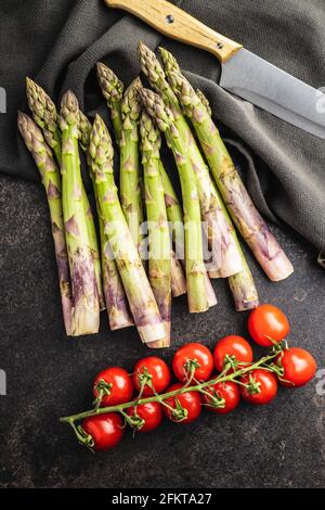 Frischer roher ungekochter grüner Spargel und Kirschtomaten auf schwarzem Tisch. Stockfoto