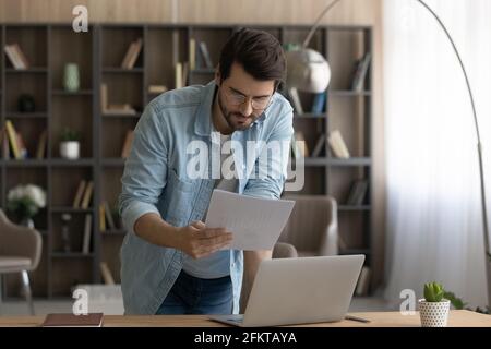 Selbstbewusster Geschäftsmann mit Brille, der Dokument liest und am Schreibtisch steht Stockfoto