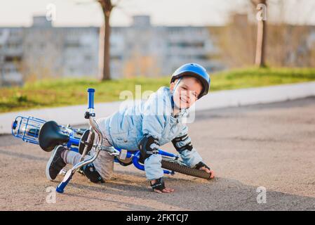 Ein kleines Kind in einem Helm und Schutz fiel von Ein Fahrrad auf den Asphalt und wurde nicht verletzt Stockfoto