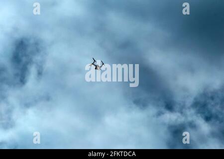 Die kleine Drohne, die hoch fliegt, ist gegen den bewölkten Himmel abgebildet. Nur die Silhouette ist sichtbar. Stockfoto