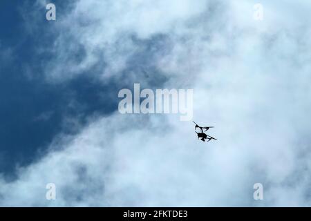Die kleine Drohne, die hoch fliegt, ist gegen den bewölkten Himmel abgebildet. Nur die Silhouette ist sichtbar. Stockfoto