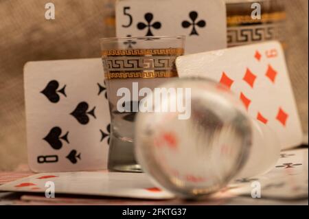 Spielkarten, ein Glas Wodka und ein Dekanterstopfen auf einem mit grobem Tuch überzogenen Tisch. Nahaufnahme, selektiver Fokus. Stockfoto