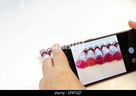 Frau macht Fotos mit dem Smartphone Tierwutimpfstoff Biocan R von Bioveta ist auf Weiß. Ampullen mit rosa Medizin innen. Tollwut-Prophylaxe. V Stockfoto