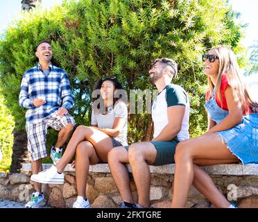 20s Gruppen von besten Freunden lachen Spaß zusammen im Stadtpark sitzen auf einer Bank reden. Zwei Studenten genießen sorglose Freude Stockfoto