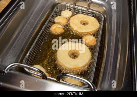 Köstliche Donuts und Donut-Löcher, die in einem Öl gekocht werden Fritteuse zeigt den leckeren Snack Braten in Öl Stockfoto