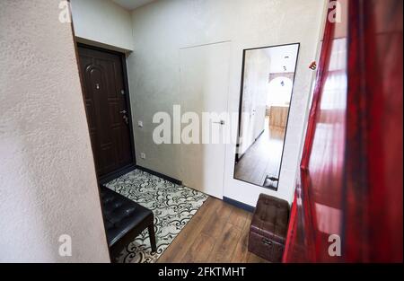 Kompakte Eingangshalle mit heller, stilvoller Einrichtung in Weiß- und Brauntönen. Rechteckiger Spiegel, Hocker und weiche Bank erfolgreich dekorieren Raum. Stockfoto