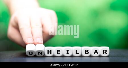 Die Hand dreht Würfel und ändert den deutschen Ausdruck „unheilbar“ (unheilbar) in „heilbar“ (heilbar). Stockfoto