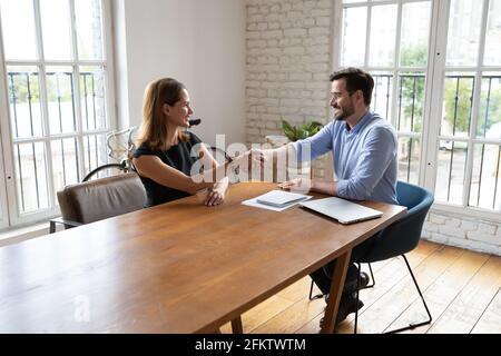 Lächelnde junge, qualifizierte Arbeitssuchende schüttelt sich die Hände mit der Personalmanagerin. Stockfoto
