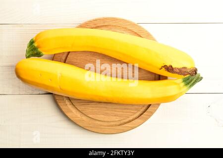 Zwei reife, saftige, organische, gelbe Zucchini, Nahaufnahme, auf einem runden Bambustablett auf einem Holztisch, Draufsicht. Stockfoto