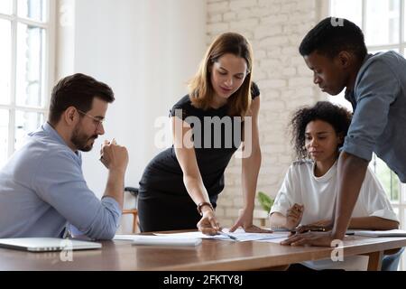 Junge Teamleiterin analysiert Statistiken mit gemischten Rennkollegen. Stockfoto