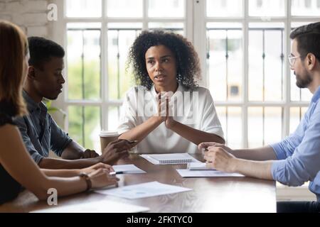 Fokussierte, multirassische Kollegen hören dem afrikanischen Führer der ethnischen Zugehörigkeit zu. Stockfoto