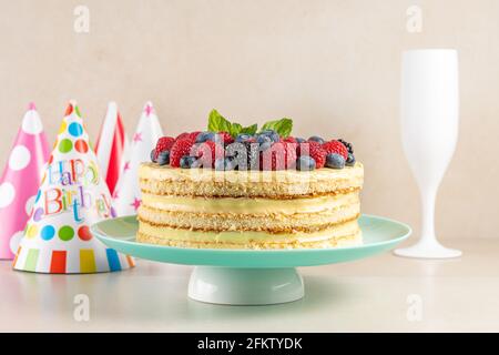 Hausgemachter Kuchen mit frischen Beeren und Geburtstagshut auf hellem Hintergrund. Stockfoto
