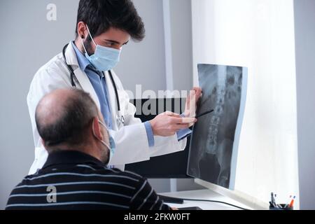 Junger Arzt, der die Röntgenaufnahme eines älteren Patienten untersucht. Radiographie einer Wirbelsäule, Wirbelsäule oder Wirbelsäule. Stockfoto