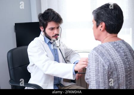 Junge Arzt Gesundheitsdienstleister Durchführung einer körperlichen Untersuchung und Hören auf reife Frau Patienten Herz und Lunge mit einem Stethoskop. Stockfoto