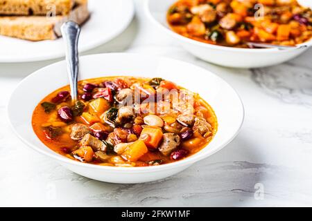 Bohnen-Suppe mit Würstchen auf weißem Teller, weißer Marmorboden. Italienisches Küchenkonzept. Stockfoto