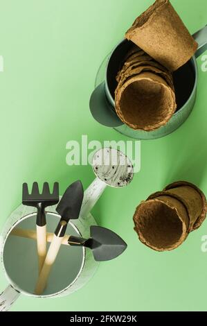 Gartenarbeit zu Hause. Anbau von Lebensmitteln auf Fensterbank. Werkzeuge, Torftöpfe und gepresster Boden für Sämlinge. Draufsicht. Flatlay auf grünem Hintergrund. Stockfoto