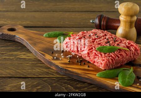 Rohes Hackfleisch auf einem Holzbrett mit Gemüse und Gewürzen. Kochen und gesunde Ernährung Konzept Stockfoto