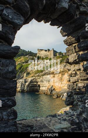 Portovenere, Italien landschaftlich reizvoller Ort an der italienischen Riviera. Byron's Grotto Blick durch eine natürliche Felsformation auf das Meer und die Burg auf dem Hügel Stockfoto