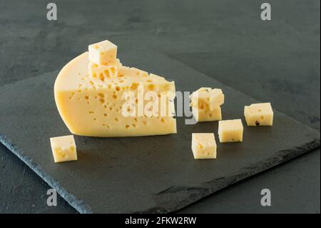 Radamer-Käse auf schwarzem Betongrund. Dreieckiges Stück gelber Schweizer Kuhmilch-Käse mit Löchern. Stockfoto