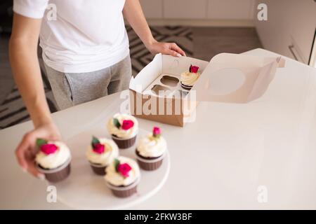 Nettes Baby Mädchen 2-3 Jahre alt essen leckere Cupcakes mit Creme auf der Oberseite in der Küche drinnen. Kindheit. Selektiver Fokus. Stockfoto