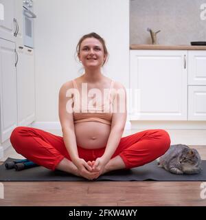 Eine Schwangerin macht zu Hause Yoga und sitzt in einem Schmetterling Pose Stockfoto
