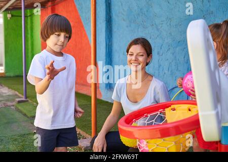 Boy wirft einen Ball ins Netz während des Basketballtrainings Mit Turnschullehrer im Kindergarten Stockfoto