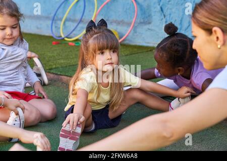 Kleines Mädchen, das sich mit anderen Kindern im Sportunterricht ausdehnt In der Kindertagesstätte Stockfoto