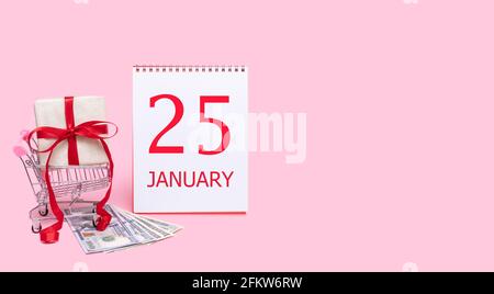 25. Tag im januar. Eine Geschenkbox in einem Einkaufswagen, Dollars und ein Kalender mit dem Datum des 25. januar auf einem rosa Hintergrund. Wintermonat, Tag der t Stockfoto