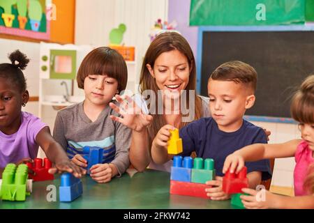 Kinder und Kindergärtnerinnen spielen mit bunten Bausteinen Das Nachschulzentrum oder die Kindertagesstätte Stockfoto