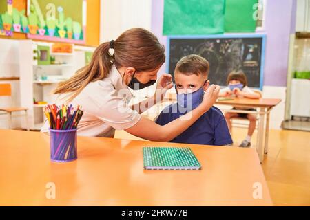 Caring Erzieher hilft Kind auf Maske im Kindergarten setzen, weil Von Covid-19 Stockfoto
