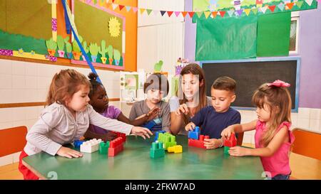 Kindergärtnerin und Kinder spielen mit Bausteinen zusammen Kindertagesstätte oder Vorschule Stockfoto