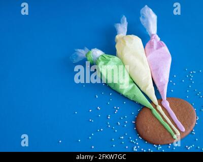 Drei Paspelsäcke mit farbiger Vereisung für die Cookie-Dekoration auf dem blauen Hintergrund, Kopierraum Stockfoto