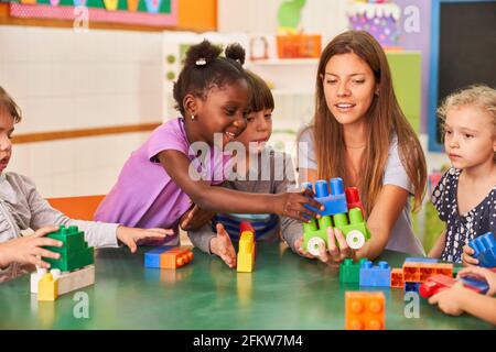 Im internationalen Kindergarten spielen Kinder mit Bausteinen zusammen Mit einer Kindergärtnerin Stockfoto