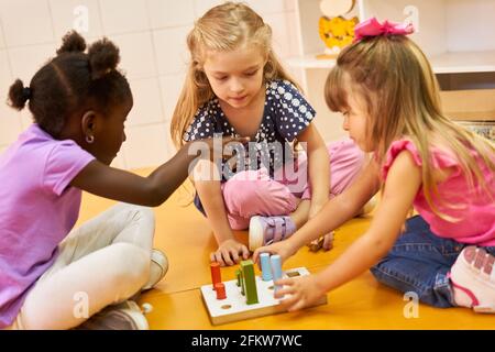Drei Mädchen im internationalen Kindergarten spielen ein Pegging-Spiel mit Bausteine Stockfoto