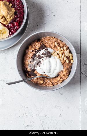 Nahaufnahme von Haferflocken-Schalen mit Schokolade, Nüssen und Joghurt, graue Fliesen Hintergrund. Gesundes Frühstückskonzept. Stockfoto