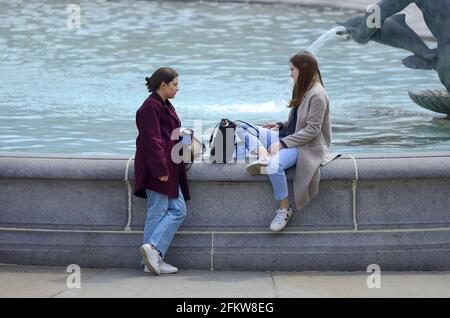 London, England, Großbritannien. Zwei junge Frauen unterhalten sich am Brunnen auf dem Trafalgar Square Stockfoto