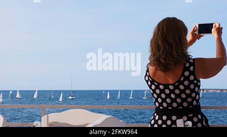 Die Frau fotografiert per Telefon den Windsurfwettbewerb auf dem blauen Meer in Sewastopol, Krim. Stockfoto