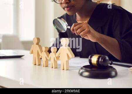 Richter mit Lupe Blick auf kleine Familienfiguren stehen Auf ihrem Tisch Stockfoto